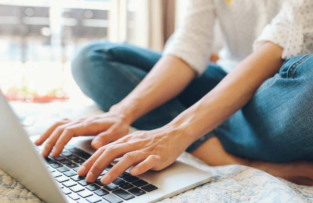 A person working on their laptop and utilizing powerful blogging tools while sitting on the floor. Learn more about conversion rate optimization for your blog.