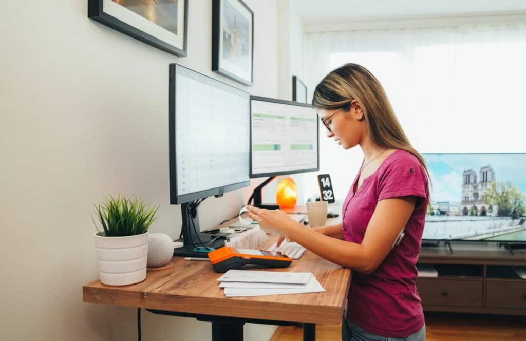 A working at a stand up desk to prevent being stagnant while writing for long periods of time. Keep reading for tips on how to write blog posts faster.
