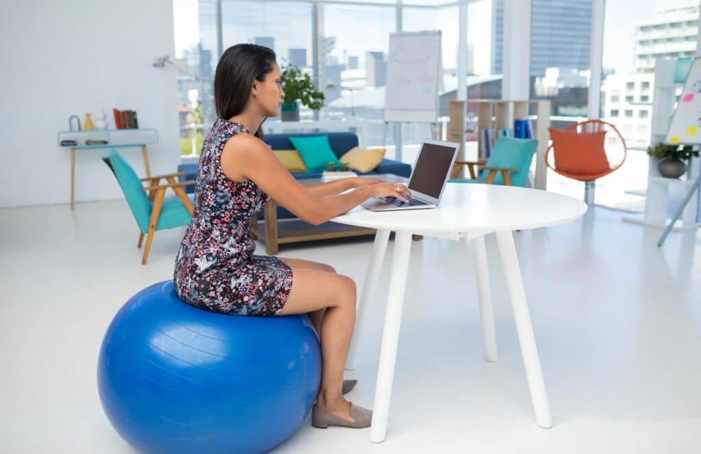 A working sitting on an exercise ball to prevent being stagnant while writing for long periods of time. Keep reading for tips on how to write blog posts faster.