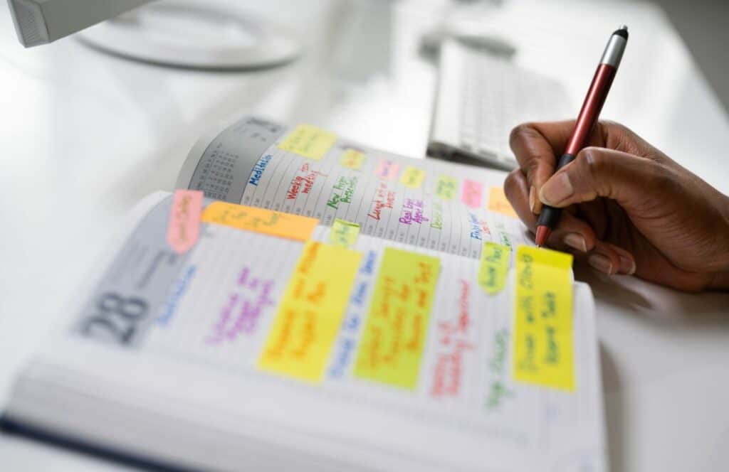 Black woman writing in a color-coded content calendar. Keep reading to learn more about the best strategies to curate content for your blog.