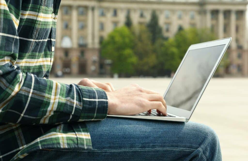 Man sitting sitting outside writing blog posts on a laptop . Keep reading to know how to write blog posts faster with a content plan.