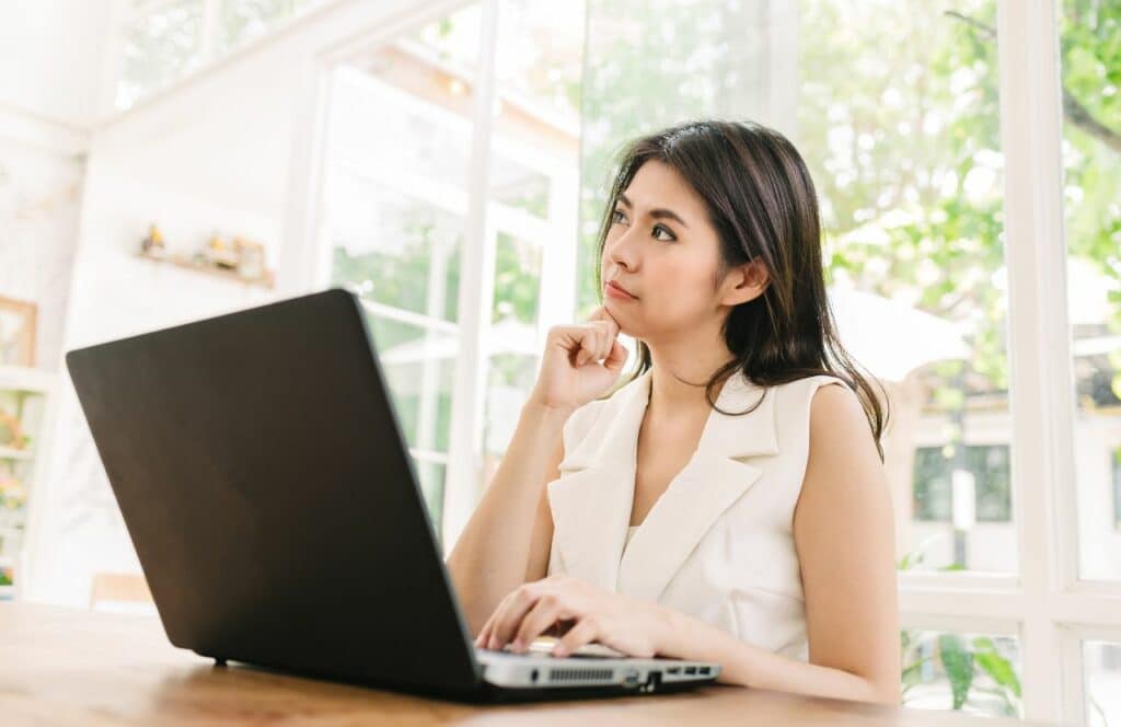Woman sitting at her desk thinking about her blog writing in small steps. Keep reading for tips on how to write blog posts faster.
