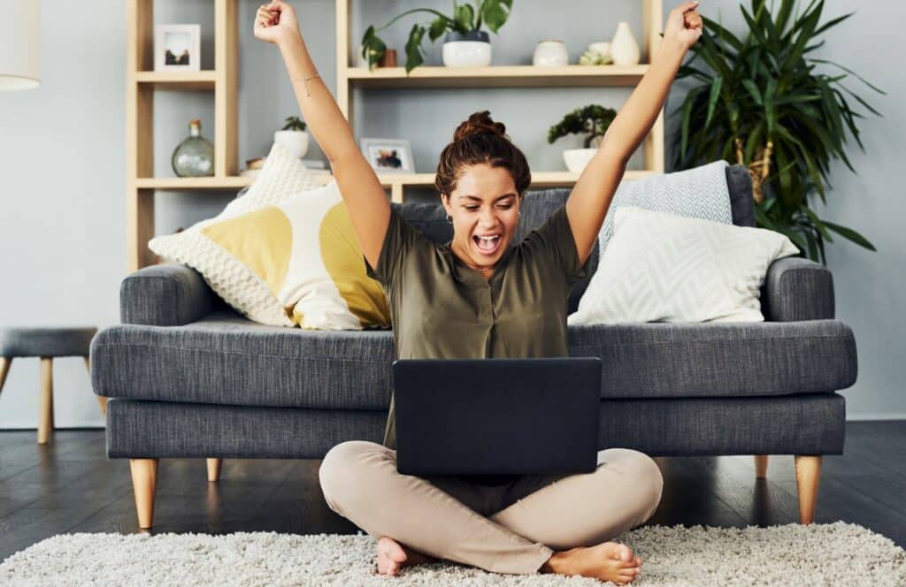 Woman sitting on the floor who is excited about writing a blog posts in record time. Keep reading for tips on how to write blog posts faster.