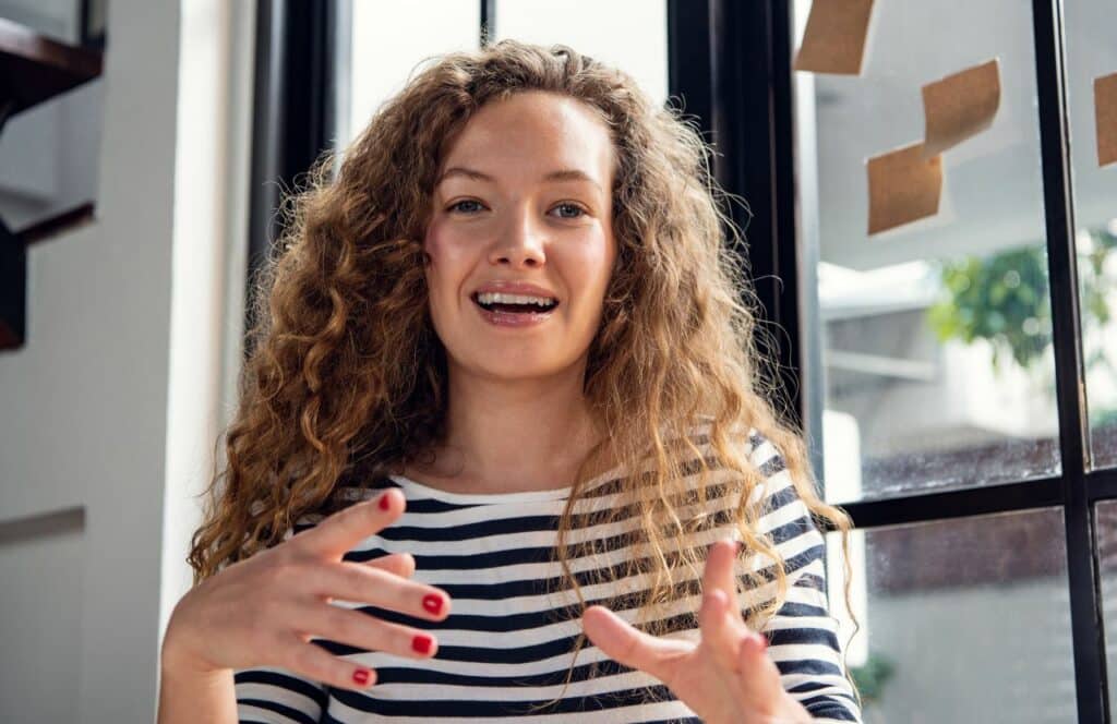Woman with curly hair having a casual conversation that can inspire you to write as you talk. Keep reading for tips on how to write blog posts faster.