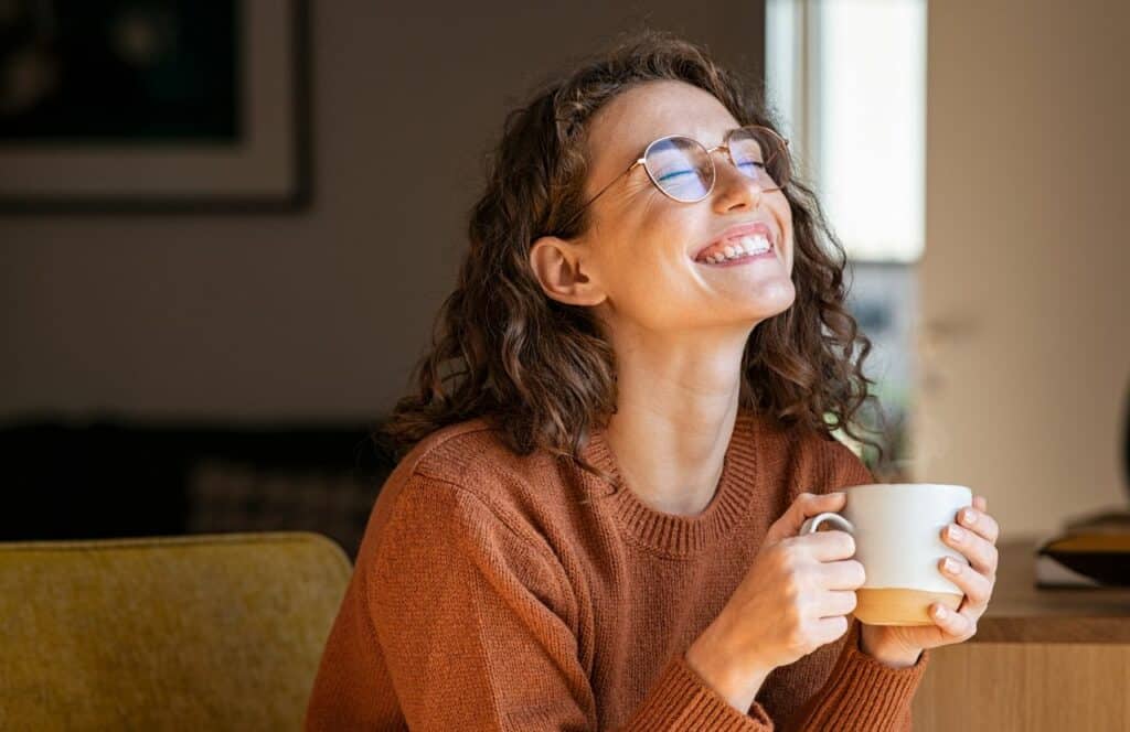 Woman with curly hair sitting on couch and taking a five minute tea break. Keep reading for tips on how to write blog posts faster.