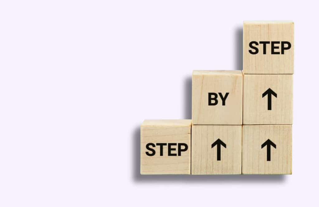 Wooden blocks stacked with the words "step by step" on them and arrows pointing up. Learn more about conversion rate optimization for your blog.