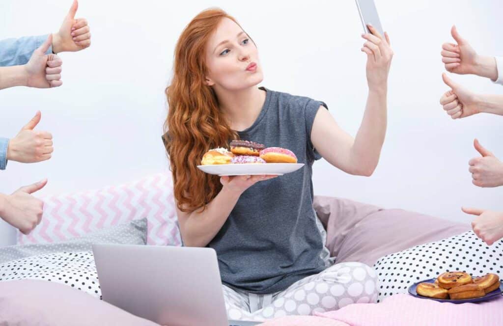 A woman with red hair holding a plate of donuts in one hand and a cell phone in the other.