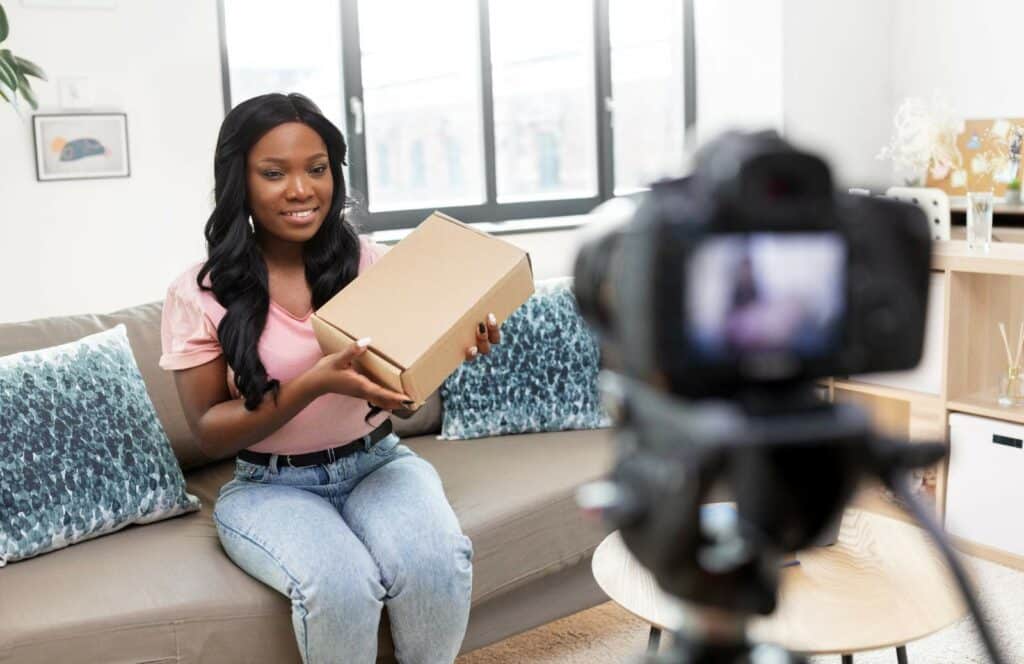 A black woman holding a box of merchandise and recording a video for her blog content. Keep reading to learn how to monetize your blog from day one as well as more about the future of blogging here.
