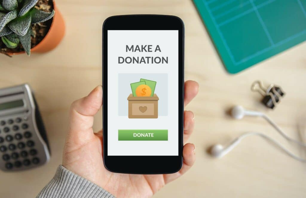 A person holding a mobile phone with a screen that reads "make a donation". Keep reading to learn how to make money blogging with donations.