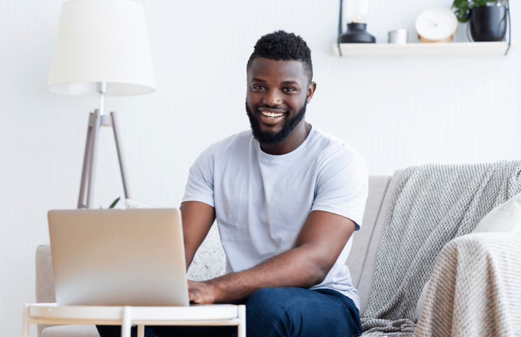 A Black man sitting on the couch blogging to demonstrate his expertise. Keep reading to learn the answer to the question, "Is Blogging Still Relevant?"