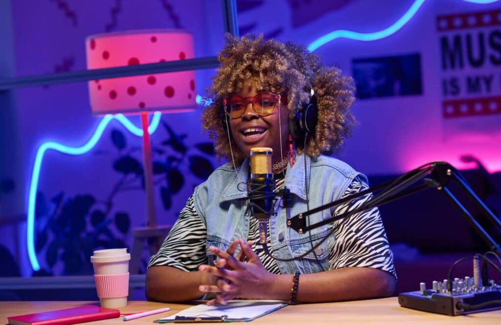 A black woman podcaster sitting in a room with a purple and pink background and sharing curated content with her blog audience