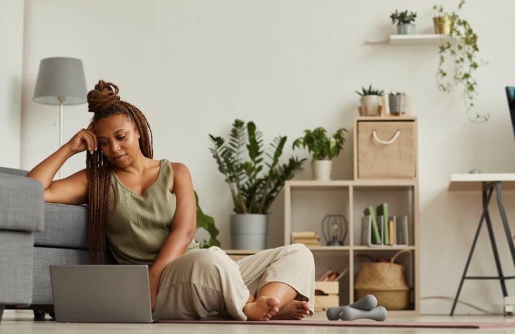 A black woman with braids sitting on the floor in her office while finishing up a blog post for her fitness blog and social media. If you have ever asked "What's the point of blogging?" click here to read more.