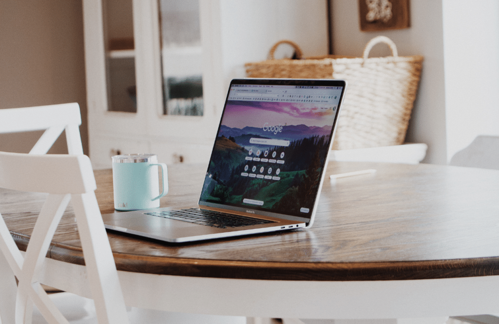 A coffee mug and laptop sitting open on a kitchen table with a Google app on the screen. Keep reading to learn the answer to the question, "Is Blogging Still Relevant?"