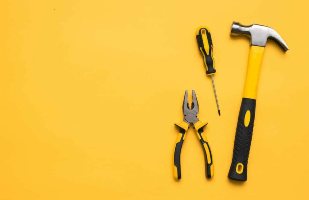 A hammer, screwdriver, and pliers laying on a yellow background signifying how bloggers needs tools to better optimize their blogging business. Learn more about the future of blogging here.
