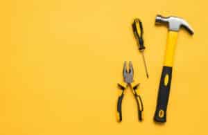 A hammer, screwdriver, and pliers laying on a yellow background signifying how bloggers needs tools to better optimize their blogging business.