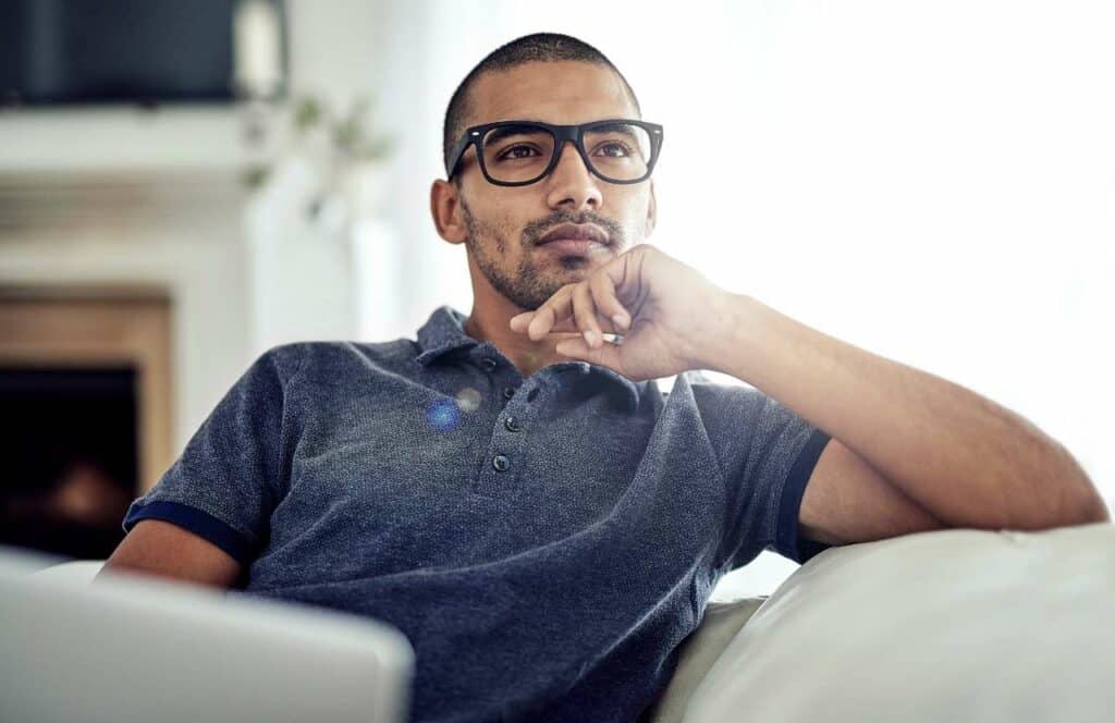 A man with glasses sitting and thinking about his blogging strategy with his laptop in his lap. Keep reading to learn more about the best strategies to curate content for your blog.