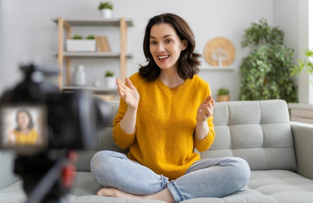 A smiling woman in a yellow sweater sitting on the floor with an inviting presence for blog readers.