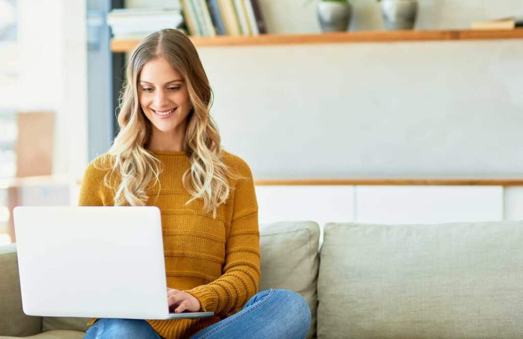 A woman in a golden colored sweat sitting on the couch while working on her professional blog. If you have ever asked "What's the point of blogging?" click here to read more.