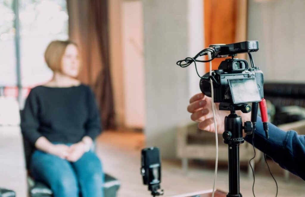 A woman sitting in front of a camera man and his equipment as she prepares to record a video for her blog audience. If you have ever asked "What's the point of blogging?" click here to read more.