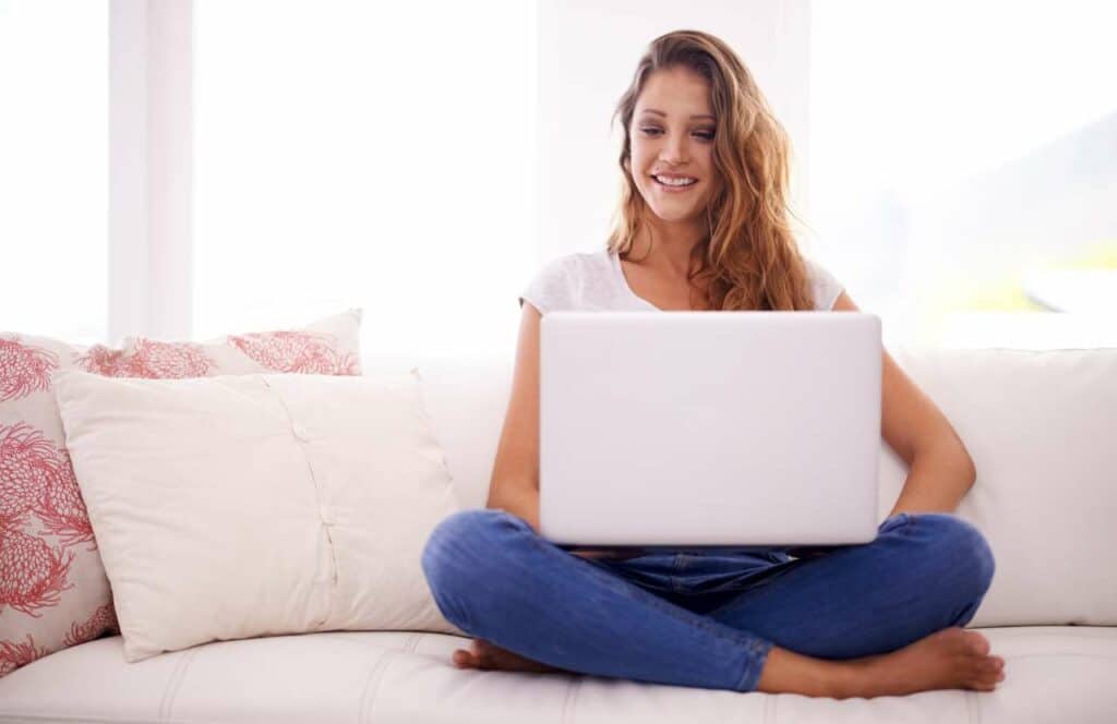 A woman sitting on her couch at home while writing valuable content for her blog business. If you have ever asked _What's the point of blogging__ click here to read more