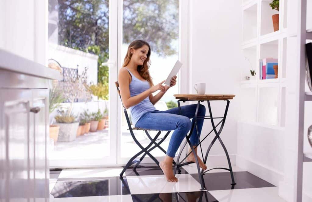 A woman sitting on in a kitchen with a checkered floor while reviewing her blog post on her ipad. If you have ever asked "What's the point of blogging?" click here to read more.