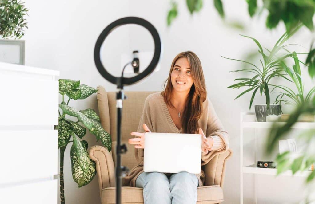 A woman sitting with her laptop, camera, and ring light as she creates content for her blog. If you have ever asked "What's the point of blogging?" click here to read more.