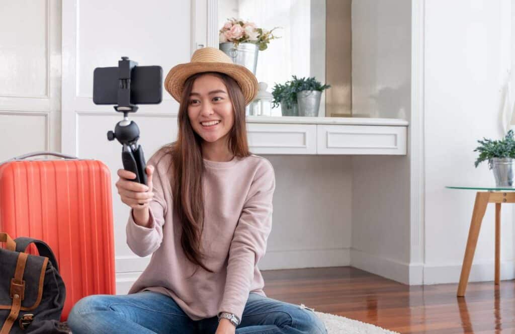 A woman with a hat on holding a camera on a selfie stick while creating a video for her blog. If you have ever asked "What's the point of blogging?" click here to read more.