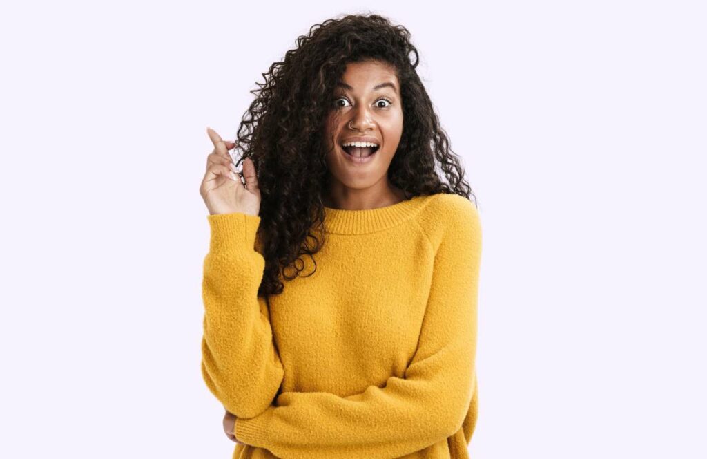 A woman with long curly hair wearing a yellow sweater looking surprised with her fingers crossed about doing the right content curation strategies for her blog. Keep reading to learn more about the best strategies to curate content for your blog.