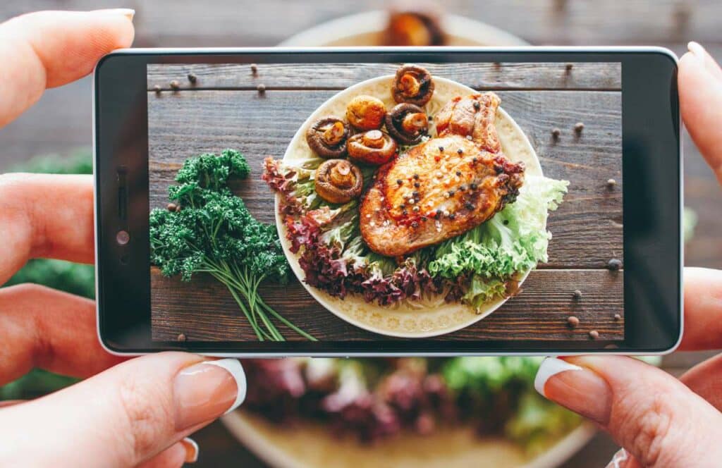 A woman's hands holding a camera and taking a picture of a beautifully plated chicken dinner for her food blog.If you have ever asked "What's the point of blogging?" click here to read more.