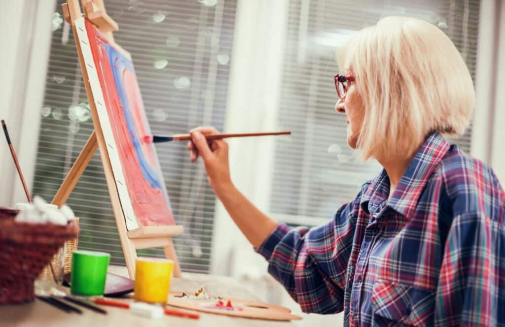 An older woman painting on a canvas as both a hobby and blogging business. If you have ever asked "What's the point of blogging?" click here to read more.