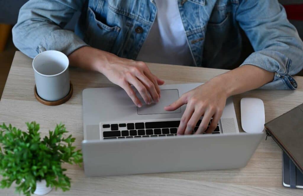 Man with a jean jacket sitting at a desk with a laptop and cup of coffee while working on his blog. Keep reading to learn more about how you can increase website conversions.