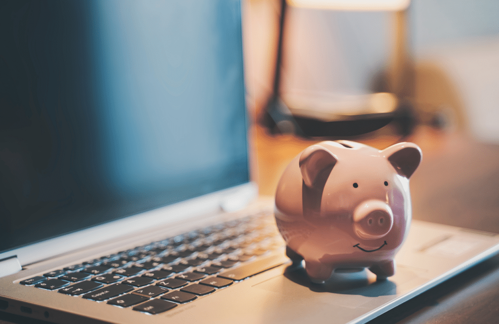 Piggy bank sitting on an open laptop of a blogger who is increasing conversions and sales by writing keyword-rich blog posts. Keep reading to learn the answer to the question, "Is Blogging Still Relevant?"