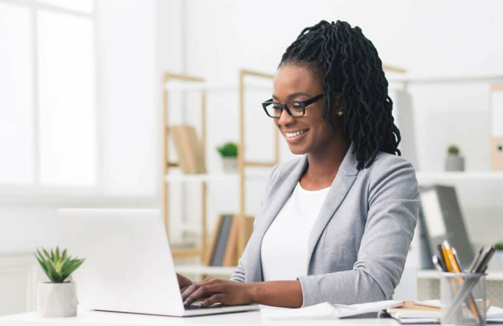 A black woman with locs, black glasses, and a gray blazer sitting at a desk while working on her blog linking strategy. Learn more about internal linking best practices by reading this blog post.
