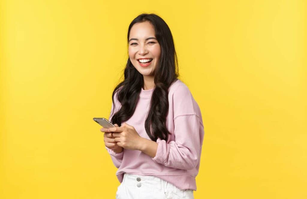 A smiling woman standing in front of a yellow background with her phone as she reads tips about blog brand awareness because content is king.