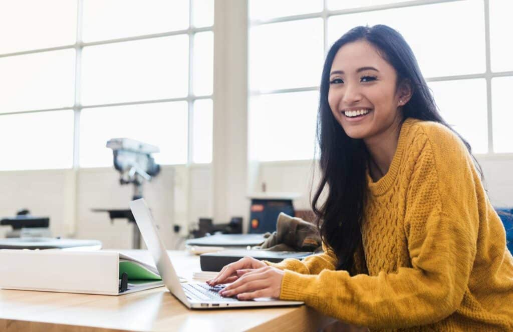 A woman in a mustard colored sweater sitting at a desk while working on her blog linking strategy. Learn more about internal linking best practices by reading this blog post.
