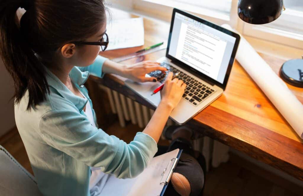 A woman sitting at a desk with a pen and her laptop while working on her blog linking strategy. Learn more about internal linking best practices by reading this blog post.