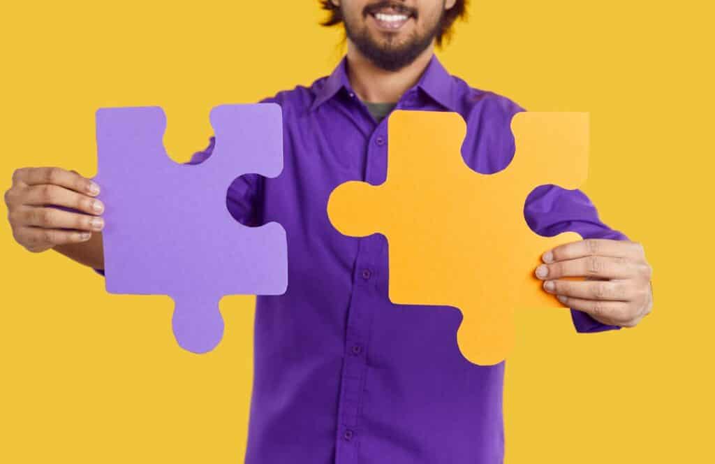 Man in purple shirt holding a purple and yellow puzzle piece in each hand. Learn more about internal linking best practices for your blog. Learn more about internal linking best practices by reading this blog post.