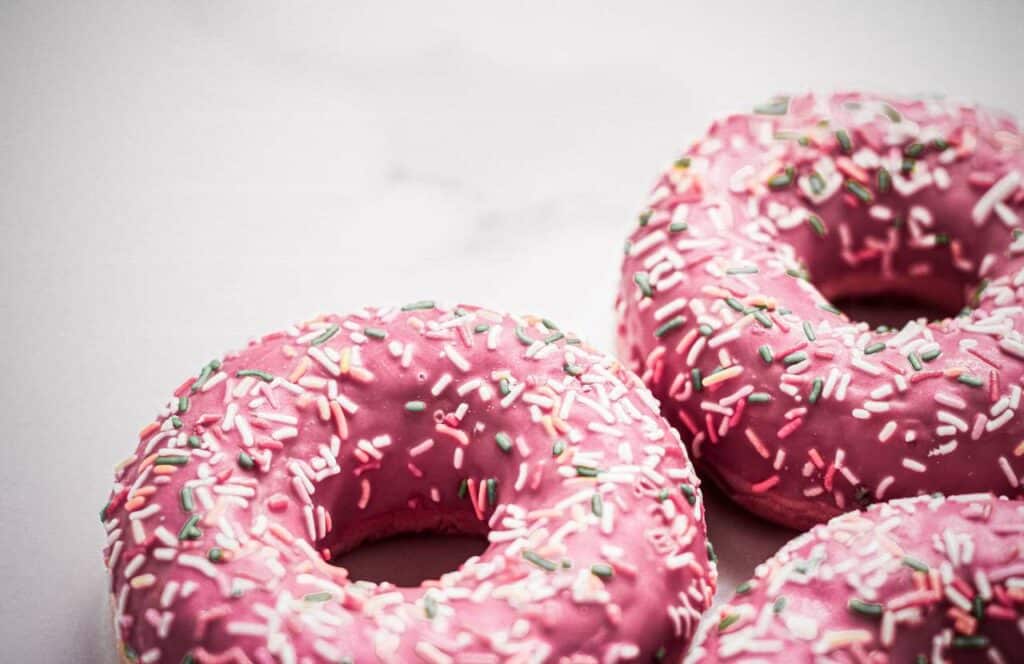 Three pink donuts with sprinkles on a white table surface. If you want to learn how to build brand awareness for your blog, then keep reading.