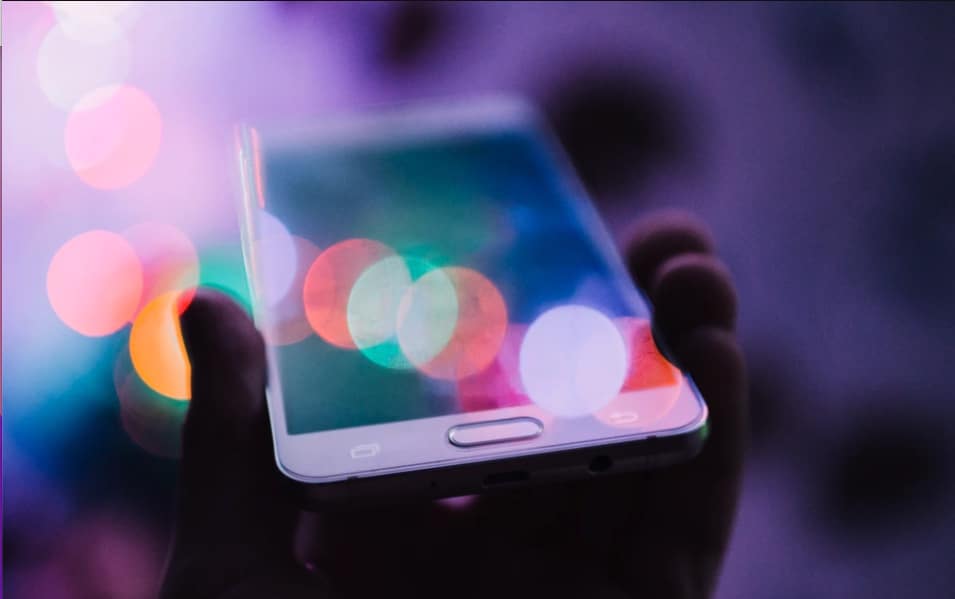 Up close shot of a person holding a cell phone with multi-colored lights reflecting off of it. If you want to learn how to build brand awareness for your blog, then keep reading.