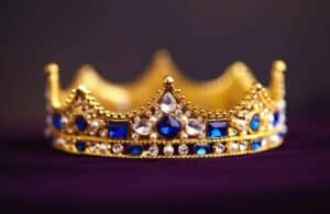 A king's crown with white and blue gems sitting on a dark purple cloth.