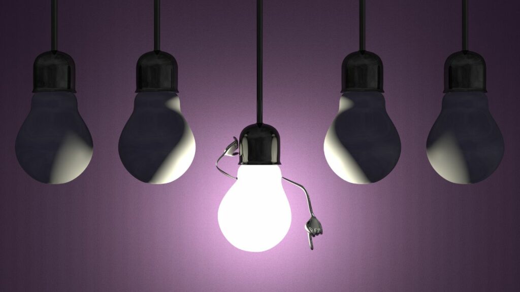 A purple light illuminates a group of hanging light bulbs. Click here to learn more about affiliate vs partner marketing for bloggers.