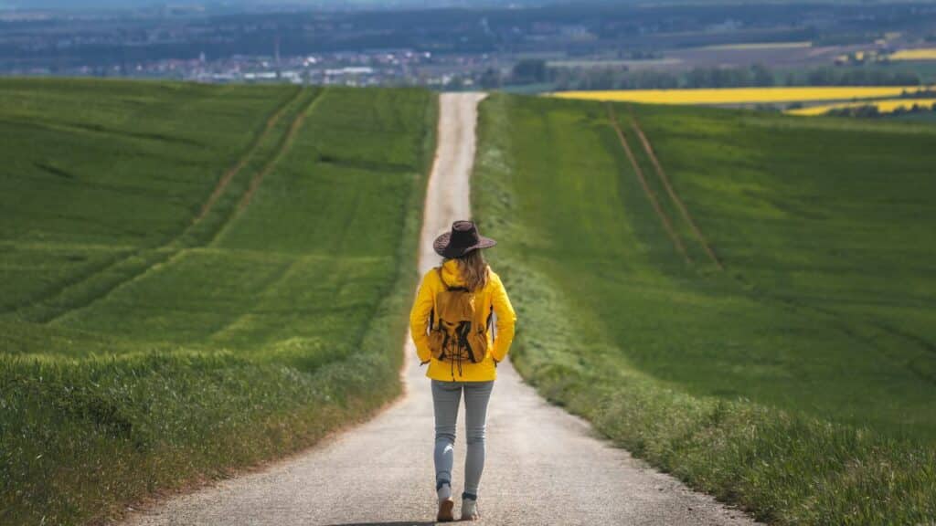 A woman walking on a country paved road surrounded by green fields and trees. Click here to learn more about affiliate vs partner marketing for bloggers.