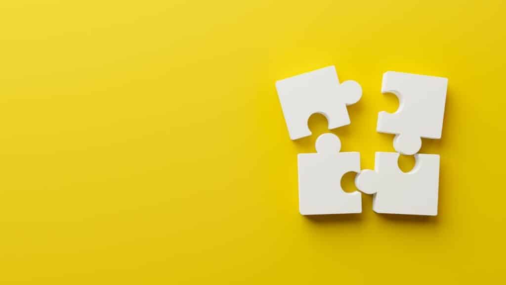 Four white puzzle pieces on a yellow background. Click here to learn more about affiliate vs partner marketing for bloggers.