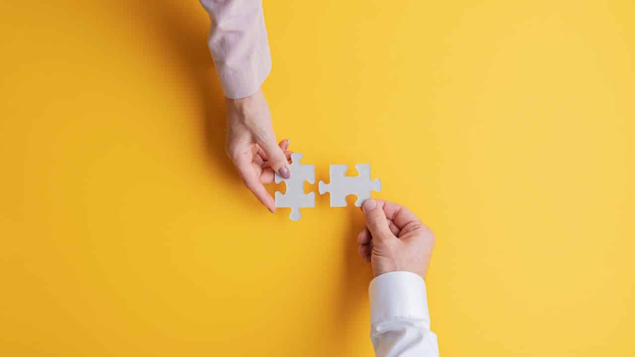Two people holding a puzzle piece on a yellow background