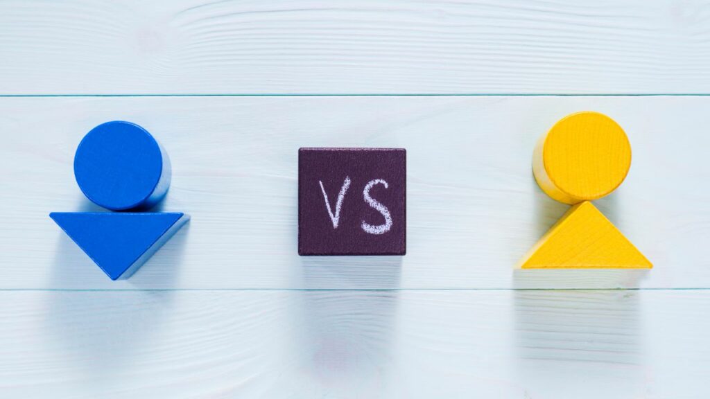 Two wooden figures stand on a block with the word versus written on it. Click here to learn more about affiliate vs partner marketing for bloggers.