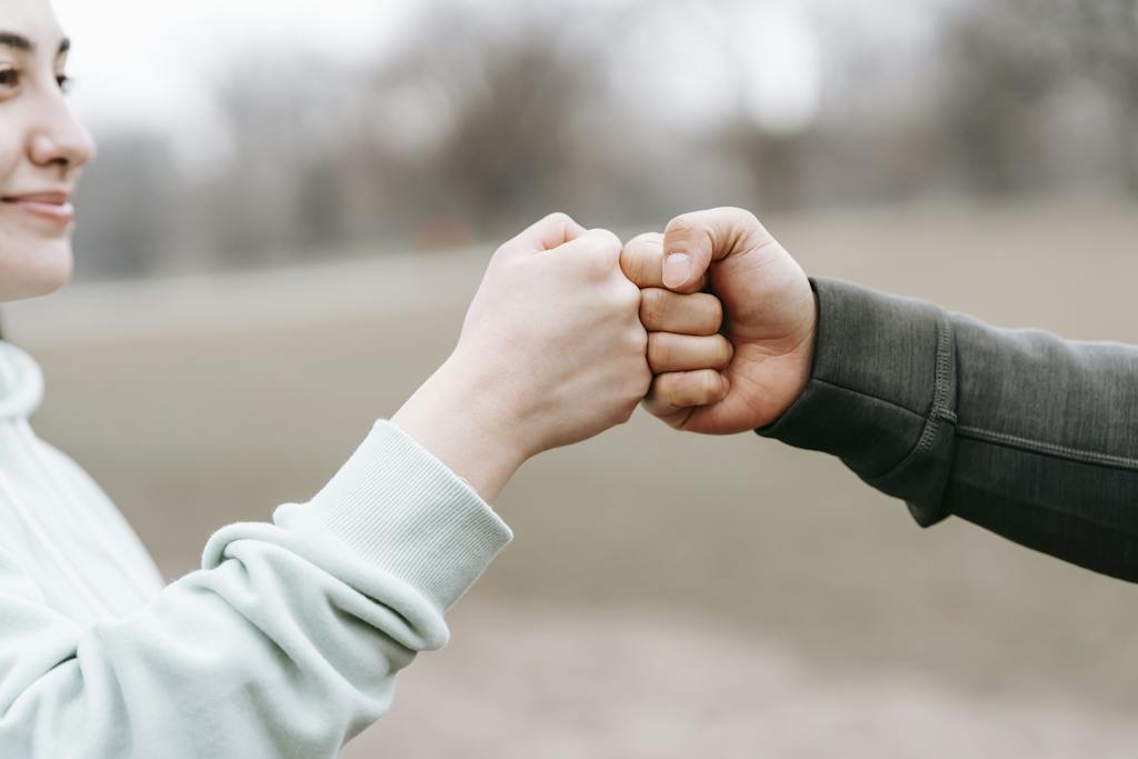 Crop anonymous cheerful woman and man giving fist bump to each other on blurred background of park